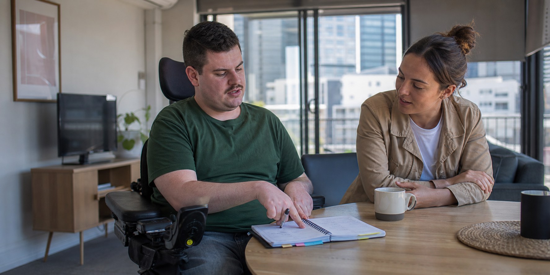 A participant using a powered wheelchair leading a household planning conversation with a support worker